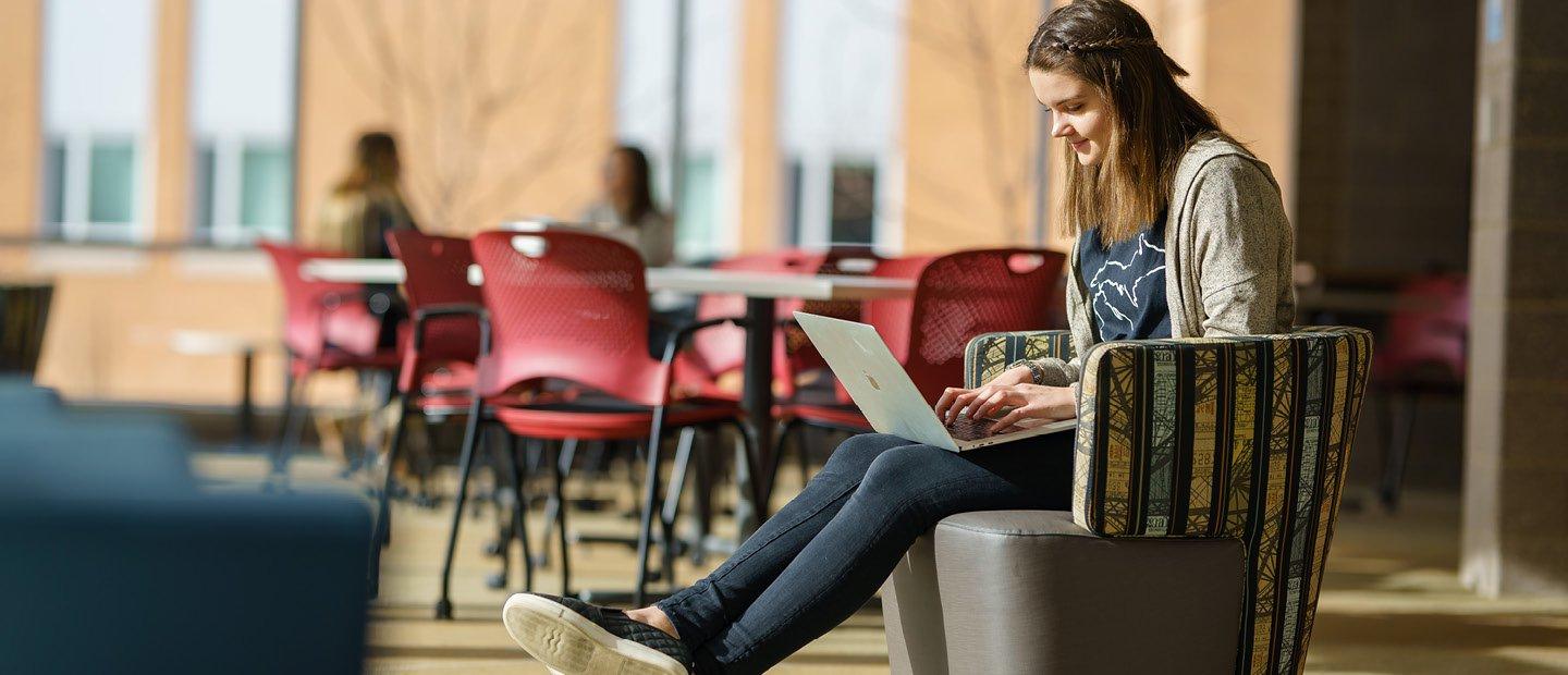 A young woman seated in a chair, typing on a laptop computer.