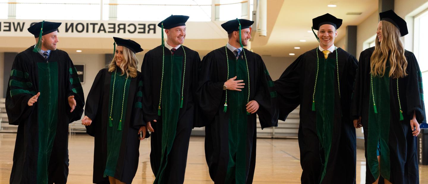 Graduates in caps and gowns walking through the Recreation Center