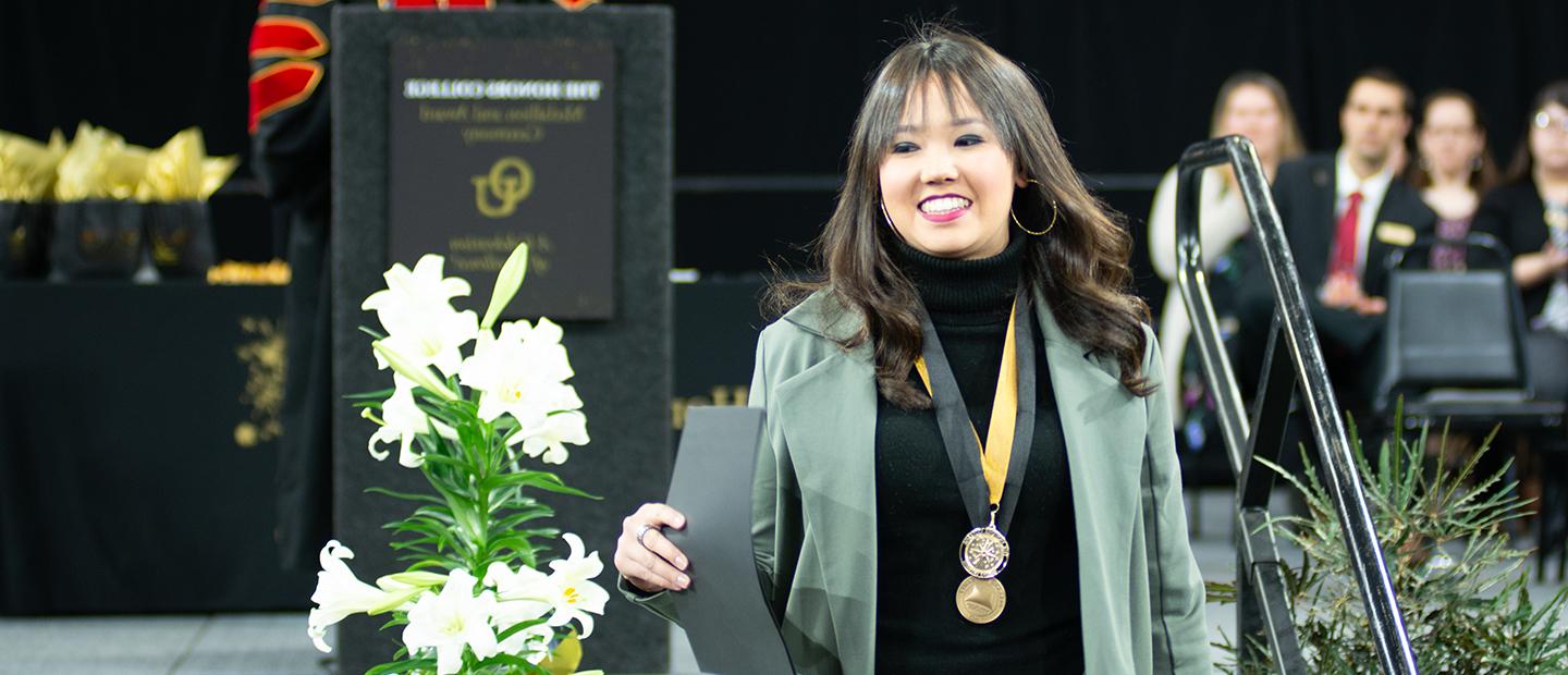 Student smiles while walking off stage after getting medallion awards at Honors College ceremony