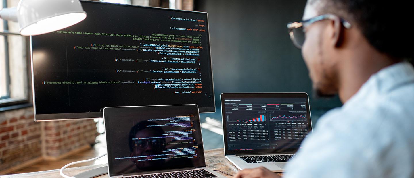 A man with two laptops and desktop in front of him