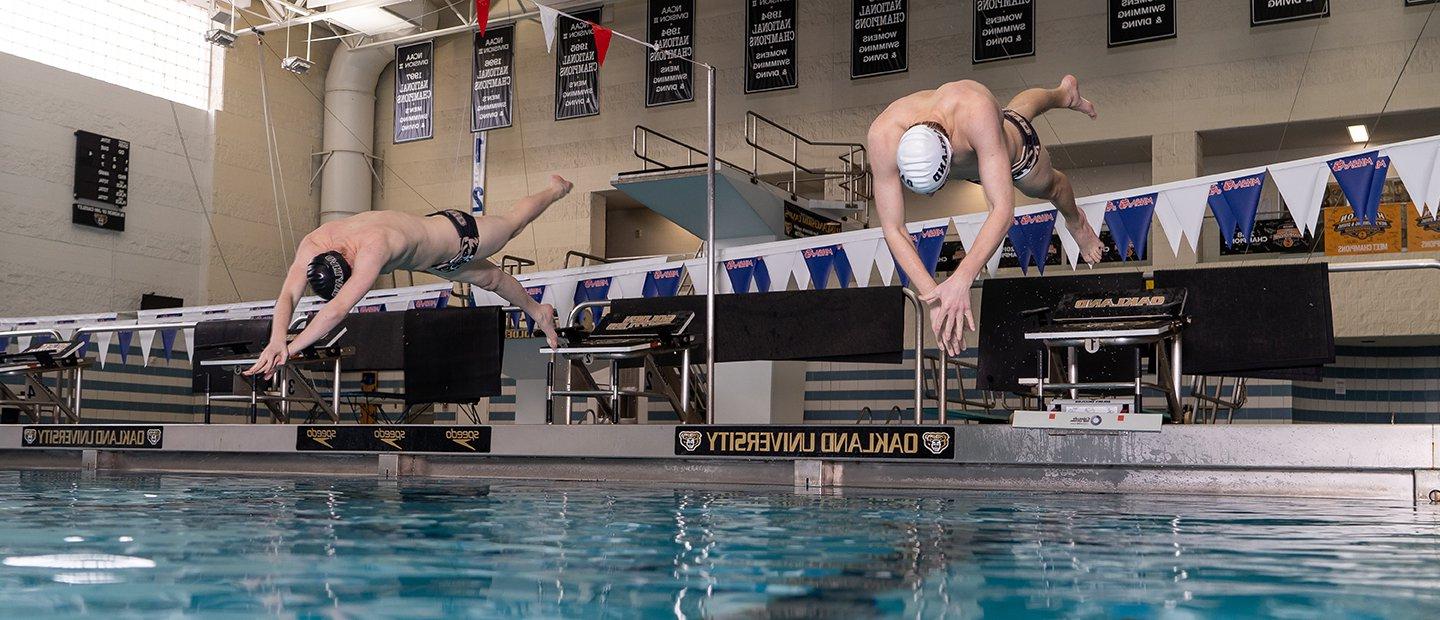 Two men diving into the swimming pool at Oakland University's aquatic center.